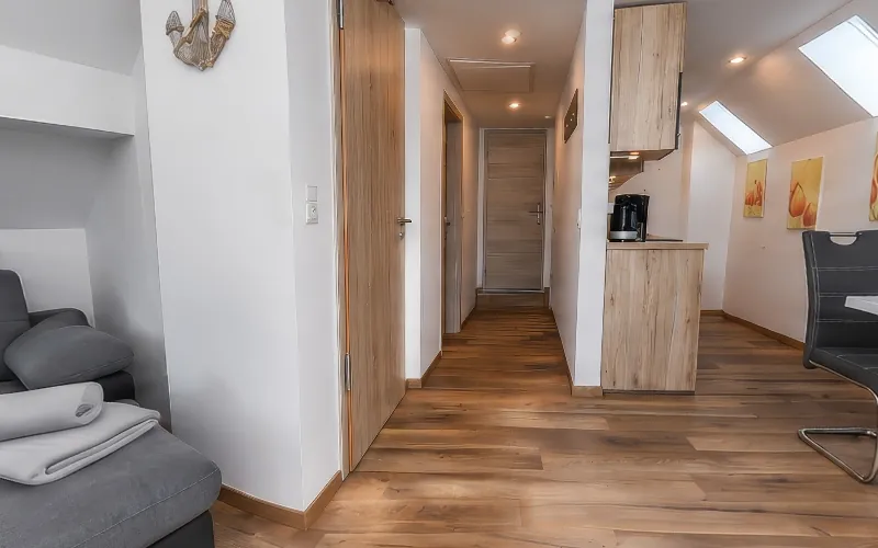 KI-generiertes Bild: Blick durch eine Ferienwohnung unter dem Dach mit Sofa, Flur, Küchenzeile und Essplatz